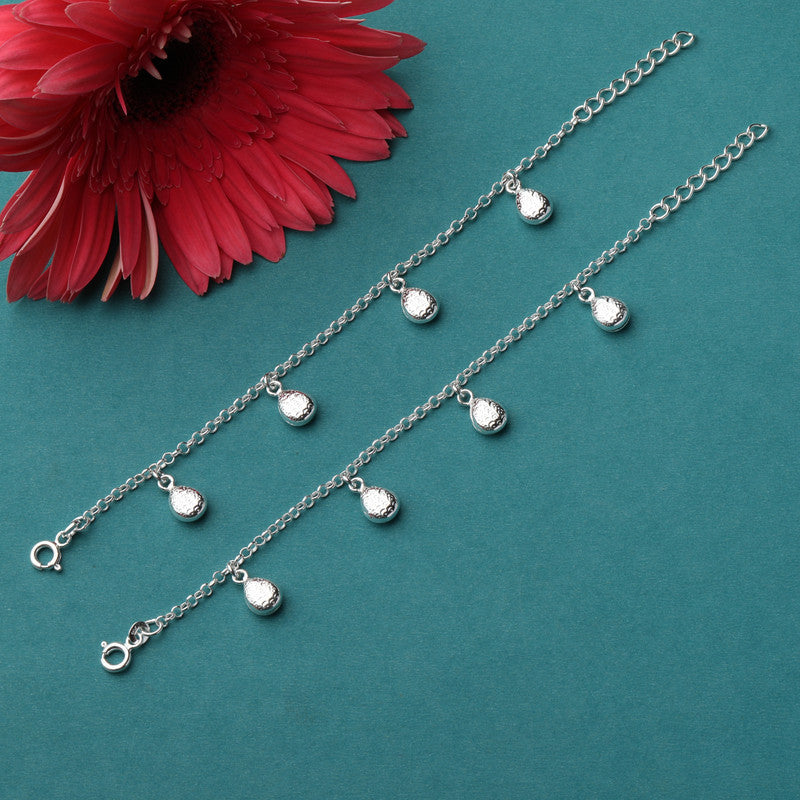 Hanging oval baby anklet displayed with props – delicate silver accessory