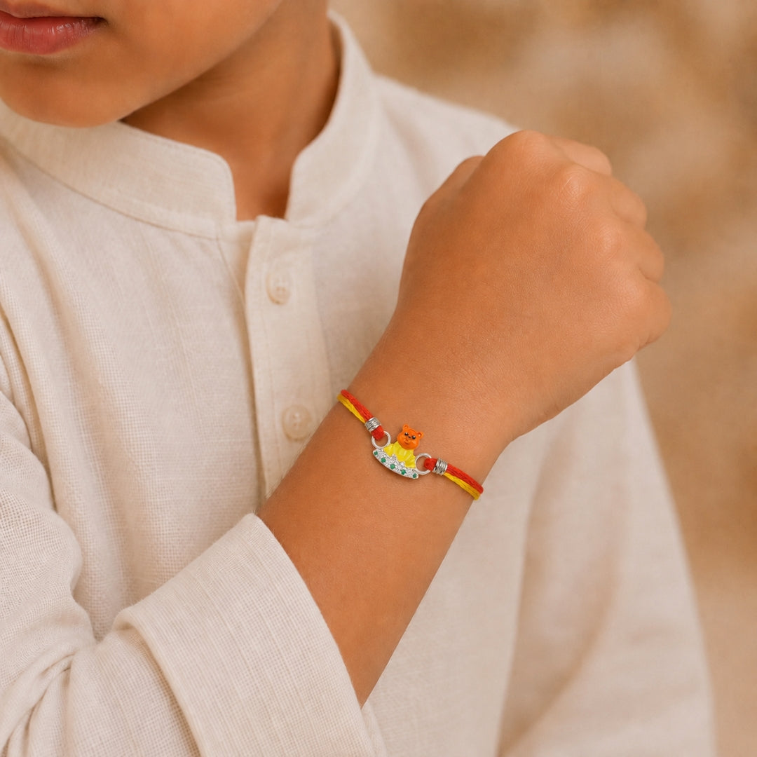 Child wearing Silver Teddy Rakhi with green stones by Silviya – cute 925 silver kids rakhi.