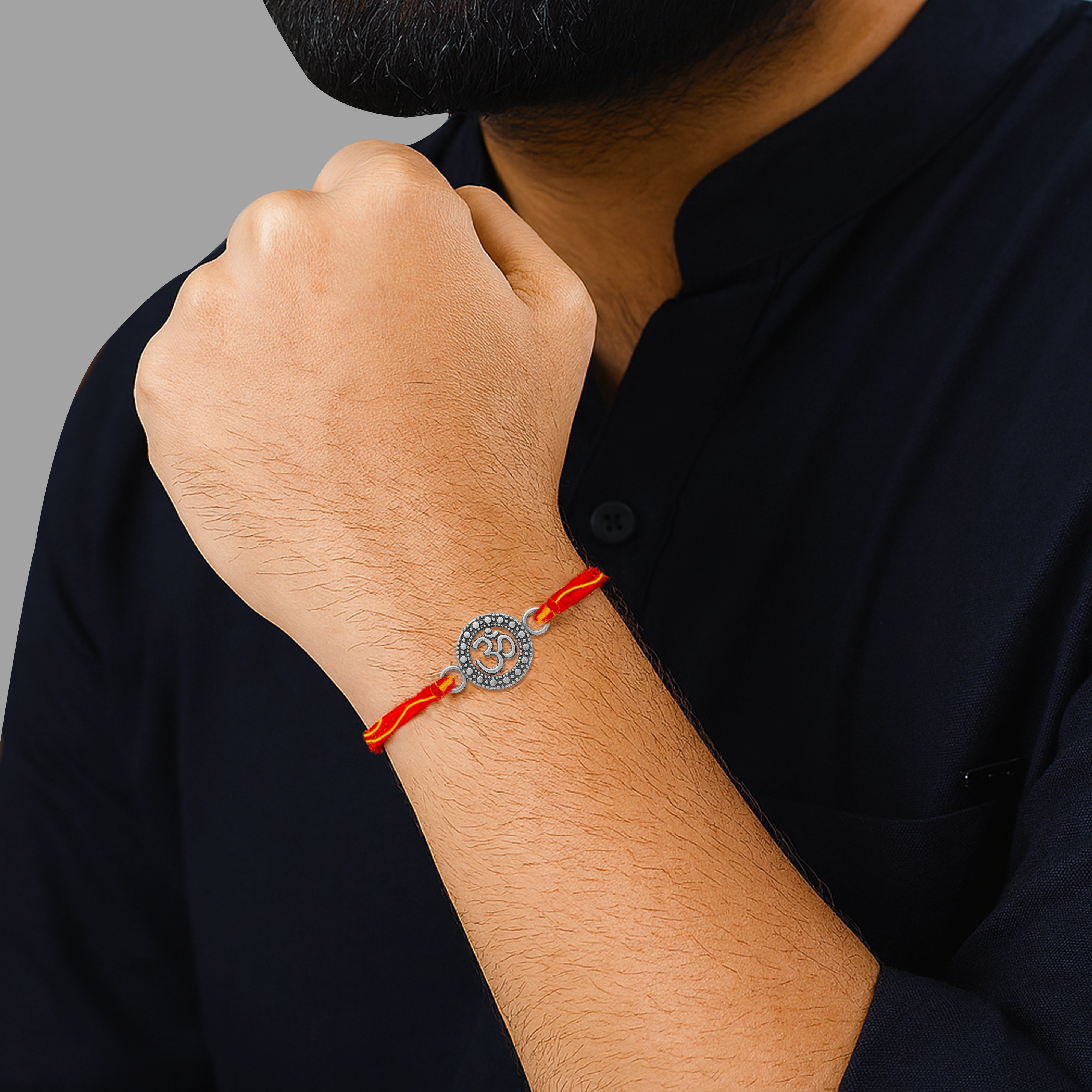 Man wearing silver Om rakhi with red thread on wrist – traditional Raksha Bandhan jewelry for brothers